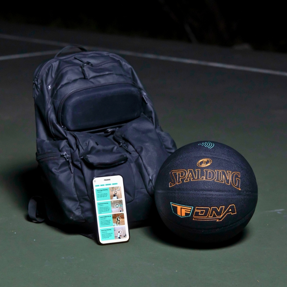 Layflat image of the Spalding TF DNA Smart Basketball next to a sleek black backpack, showcasing the complete training bundle. The premium basketball features advanced internal sensor technology designed to track shots and performance through the TF DNA app.